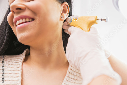 Fotografie Cropped photo of a smiling woman patient getting ear piercing procedure by a specialist in medical gloves in the cosmetologist cabinet