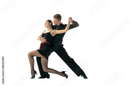 Beautiful sportive young man and woman dancing Argentine tango isolated on white studio background. Artists in black stage costumes