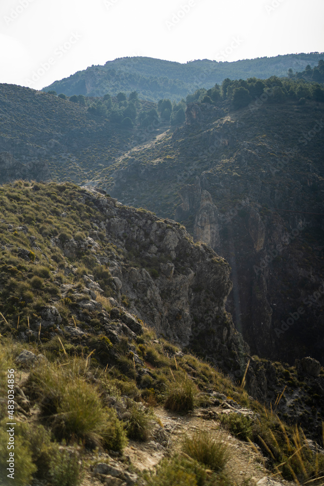 Obraz premium Paisaje de la sierra de Granada con tonos verdes y cielo despejado con nubes bajas agregando neblina a la escena 