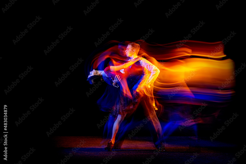 Dynamic portrait of young ballroom dancers dancing Argentine tango isolated on dark background with neon mixed light. - obrazy, fototapety, plakaty 