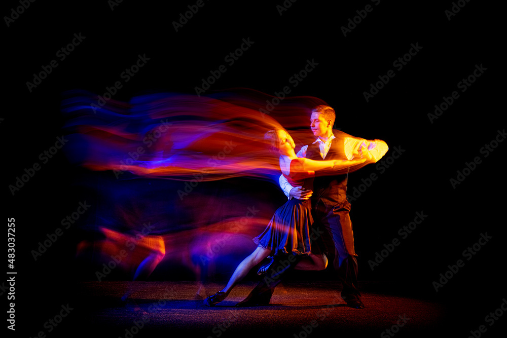 Dynamic portrait of young ballroom dancers dancing Argentine tango isolated on dark background with neon mixed light. Dynamic portrait of young ballroom dancers dancing Argentine tango isolated on dark background with neon mixed light.