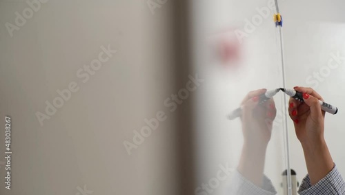 Close-up hands of unrecognizable business woman writing ideas on white board in meeting room. Tracking shot of female employee holding marker drawing on whiteboard working on project plan.