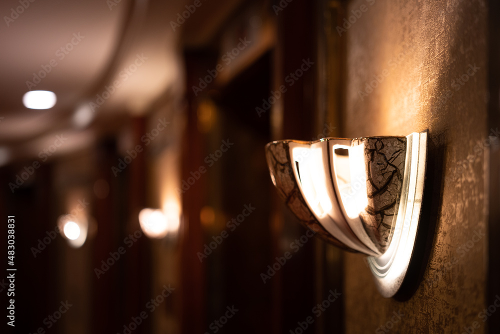 A classic luxury designed wall lamp with blurred background of corridor walk way. Interior decoration object with selective focus. Photo contained high contrast ratio between light and shadow area.