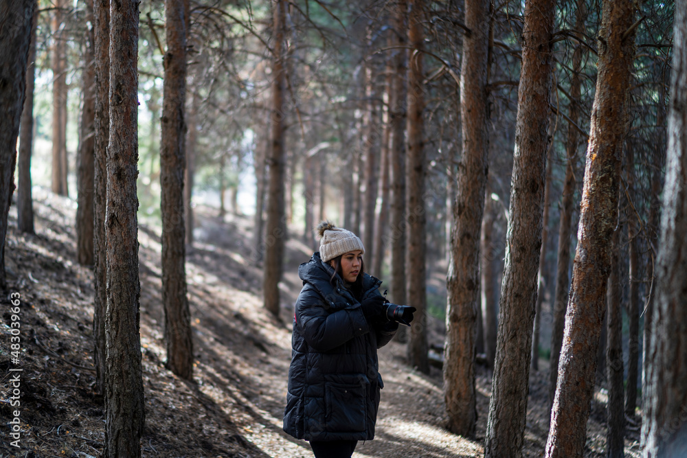 Chica joven guapa en un bosque de arboles altos con cámara de foto colgada al cuello Chica joven guapa en un bosque de arboles altos con cámara de foto colgada al cuello