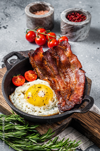 English breakfast with fried egg and bacon in cast iron pan. Gray background. Top view