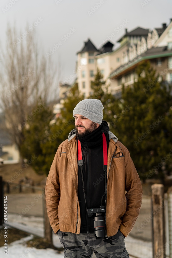 Chico joven alto con barba en ciudad nevada y cámara de fotos colgada Chico joven alto con barba en ciudad nevada y cámara de fotos colgada