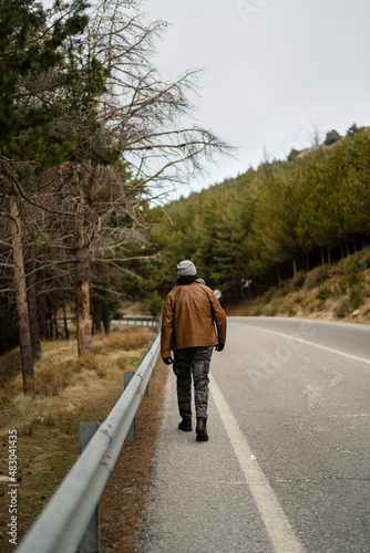 Chico alto con barba de espaldas caminando por una carretera con entorno nevado y natural