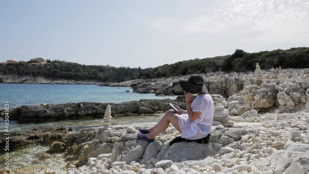 Female Vacationist In Sun Hat Sitting At The Rocky Coast Of Emplisi Beach In Erisos, Greece. - static Female Vacationist In Sun Hat Sitting At The Rocky Coast Of Emplisi Beach In Erisos, Greece. - static