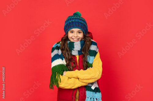 glad teen girl in knitted winter hat and scarf on red background, season fashion