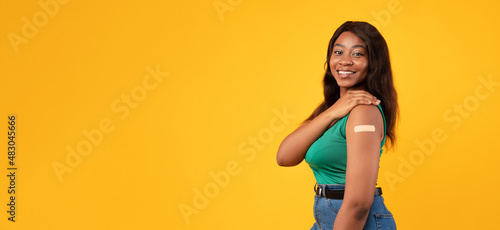 Happy Vaccinated Black Lady Showing Arm With Plaster, Yellow Background © Prostock-studio