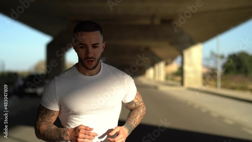 Chico joven atractivo tatuado con camiseta blanca corriendo por la carretera 