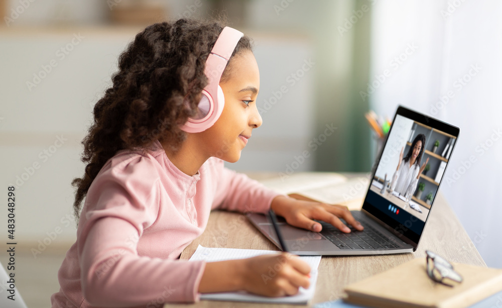 Little african american kid female in headphones doing homework and watching lesson with millennial woman on laptop Little african american kid female in headphones doing homework and watching lesson with millennial woman on laptop