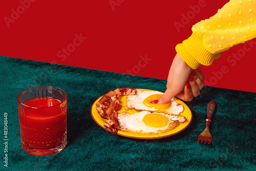 Human hand tasting bacon and eggs isolated on green and red background. Vintage, retro style interior. Food pop art photography. photo