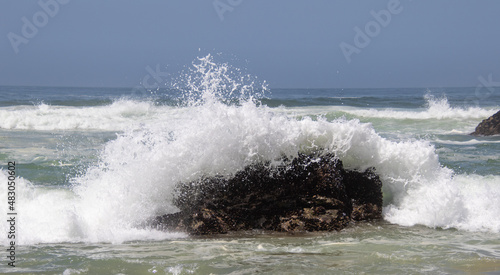 Wave breaks over a large dark rock in the ocean