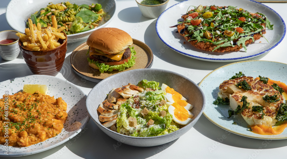 Gourmet foods on the table include burgers, pasta, french fries, vegetable salad, chicken salad, cauliflower, macaroni Gourmet foods on the table include burgers, pasta, french fries, vegetable salad, chicken salad, cauliflower, macaroni