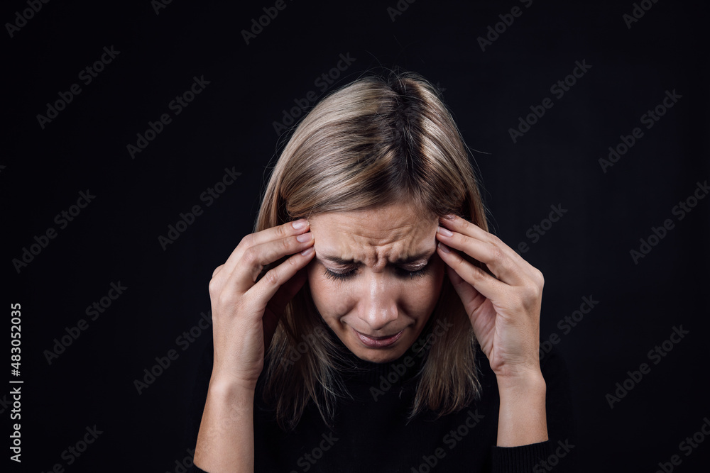 Portrait of crying woman with face down hand fingers touching temples on black background. Victim of physical and psychological abuse. Gaslighting. Relative aggression. Portrait of crying woman with face down hand fingers touching temples on black background. Victim of physical and psychological abuse. Gaslighting. Relative aggression.