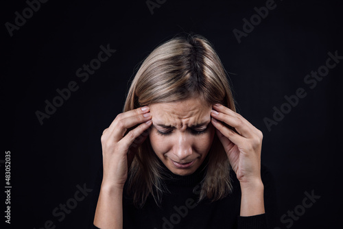 Portrait of crying woman with face down hand fingers touching temples on black background. Victim of physical and psychological abuse. Gaslighting. Relative aggression. photo