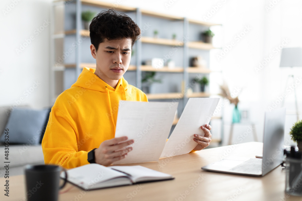Man holding paper reading report working on laptop at home Man holding paper reading report working on laptop at home