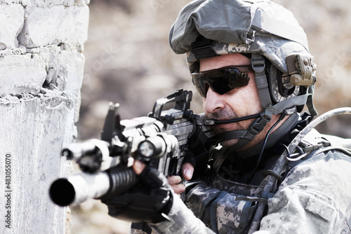 Taking aim. A soldier crouched down next to a broken down wall and pointing his gun into the distance.