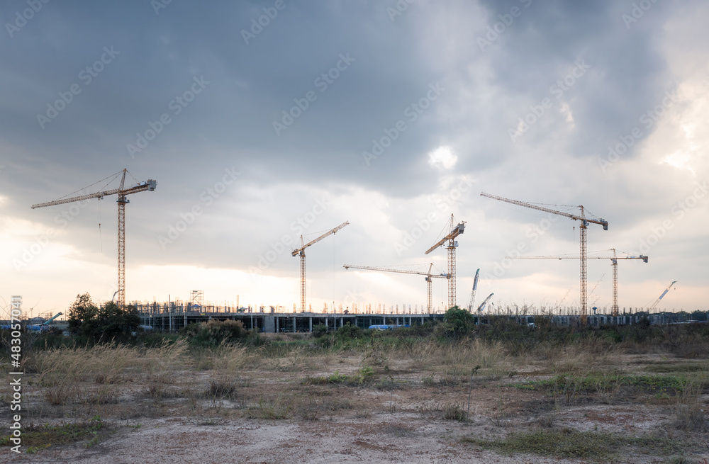 Construction site with sunset sky background at evening consist of concrete structure of building, tower crane or equipment and scaffolding. Large project to development city by engineering technology