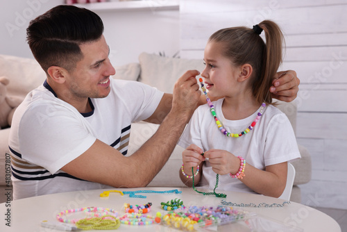 Photography Happy father putting handmade beaded jewelry on his cute daughter at home