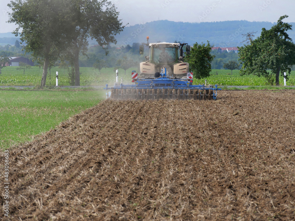 Fototapeta premium On a field in Wennerode am Harz in the state of Lower Saxony, a tractor is cultivating heavy Harz arable land with a heavy-duty cultivator. .