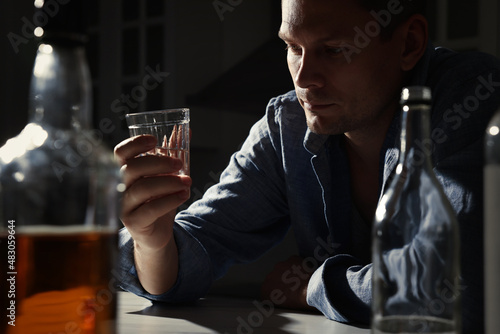 Addicted man with alcoholic drink at table in kitchen