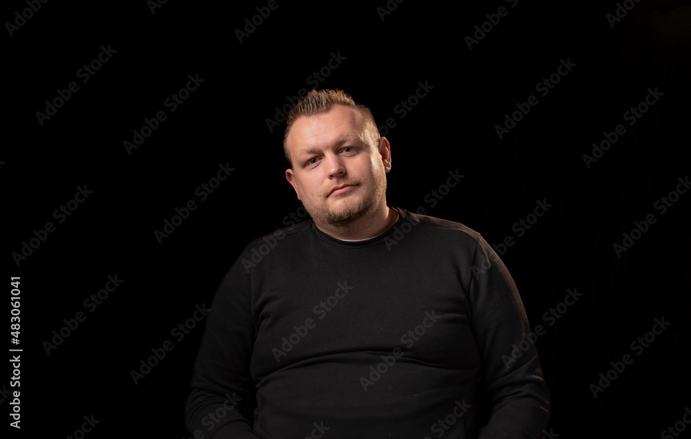 Portrait of a young man with a beard. Dark background. A slightly overweight man with a large build.
