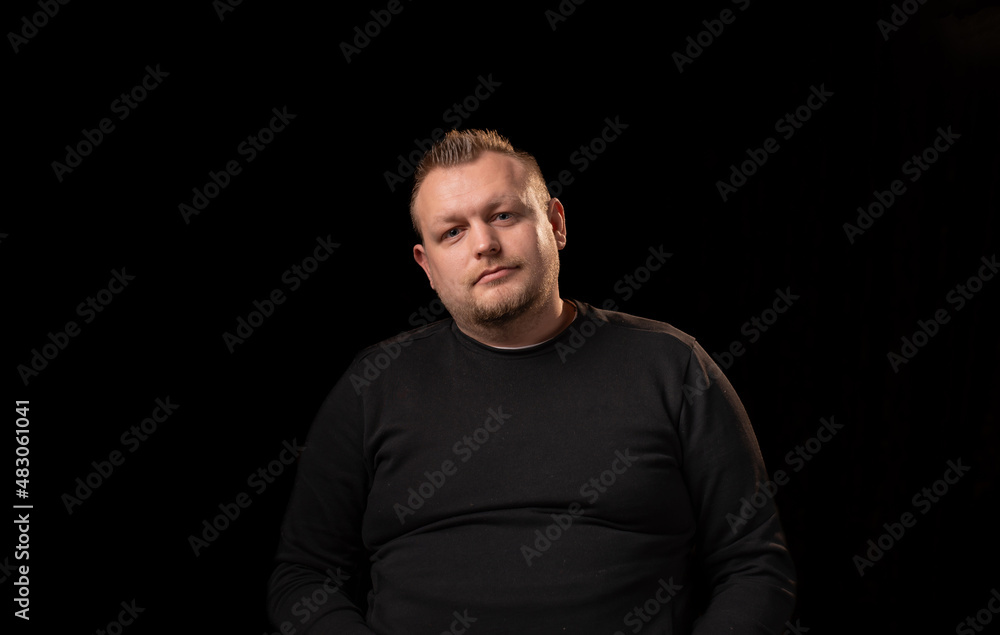 Portrait of a young man with a beard. Dark background. A slightly overweight man with a large build. Portrait of a young man with a beard. Dark background. A slightly overweight man with a large build.