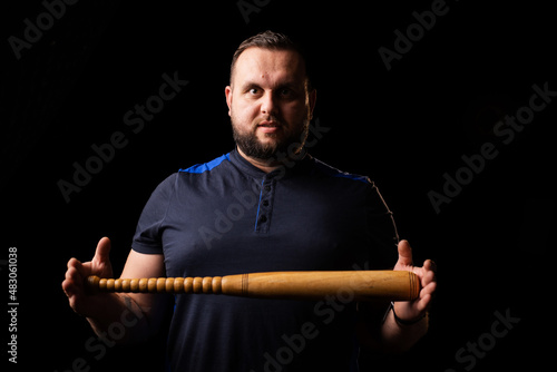 A young man is holding a wooden bat. Bouncer, security guard, bodyguard concept. A large man in a T-shirt looks at the camera.
