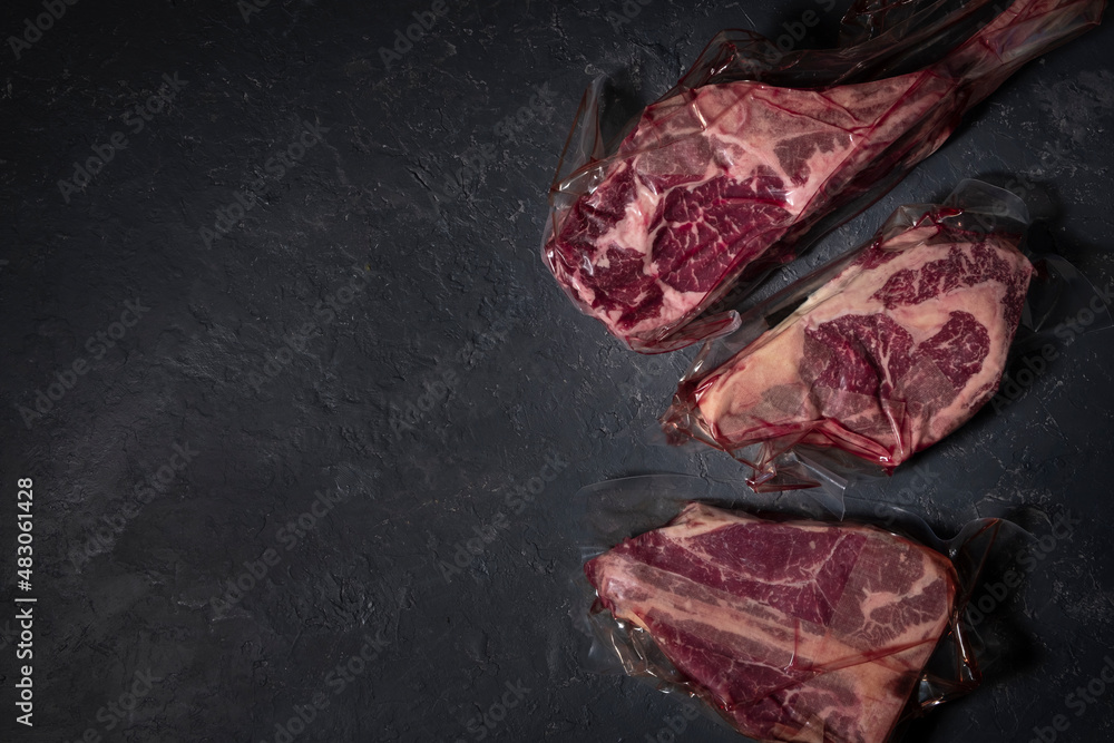Three types of steak in vacuum packaging on a dark background. Top view