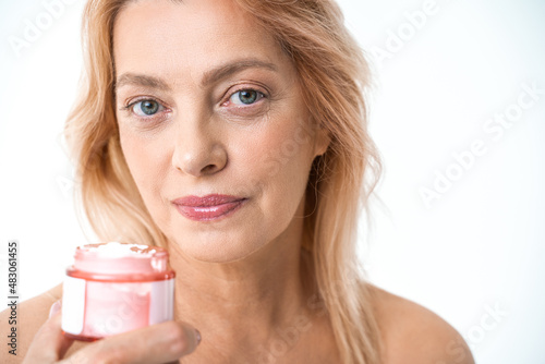 Elderly woman holding jar with moisturizing cream at her hands