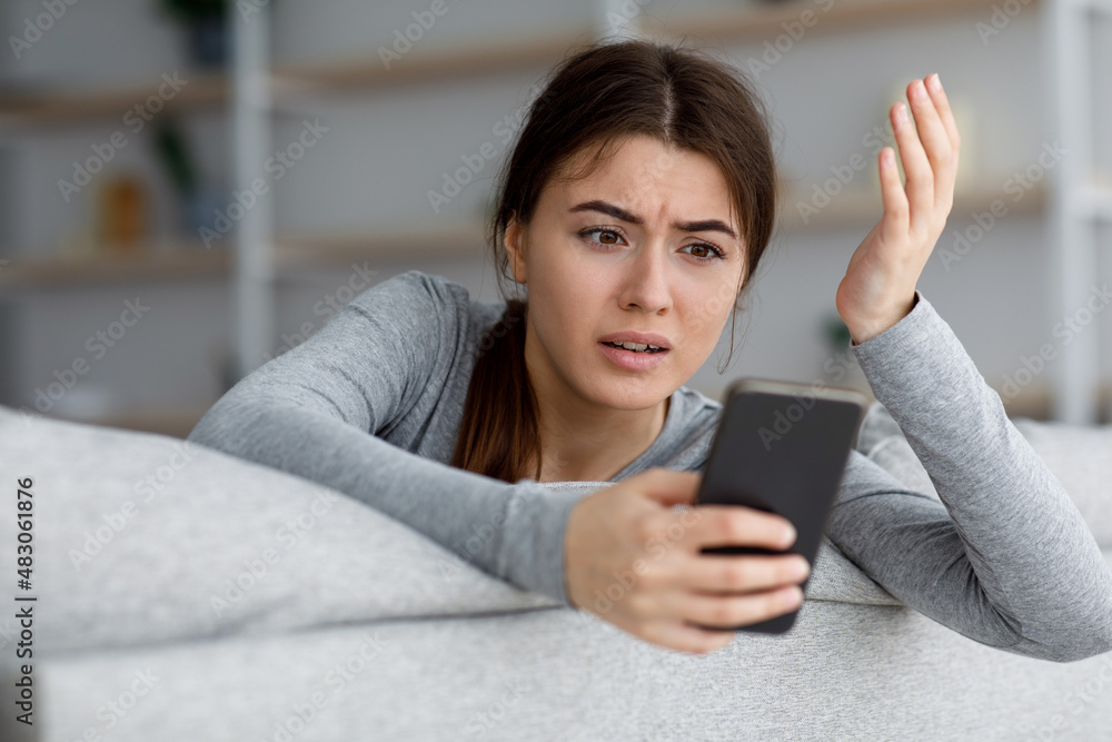 Angry sad shocked depressive attractive young caucasian female looking at phone and gesturing Angry sad shocked depressive attractive young caucasian female looking at phone and gesturing