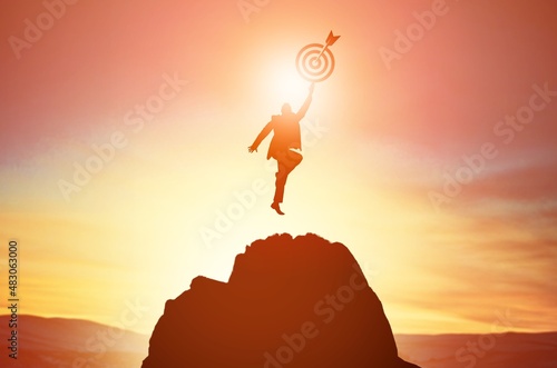 Silhouette of businessman holding a target board on top of mountain. Concept of objective achievement.