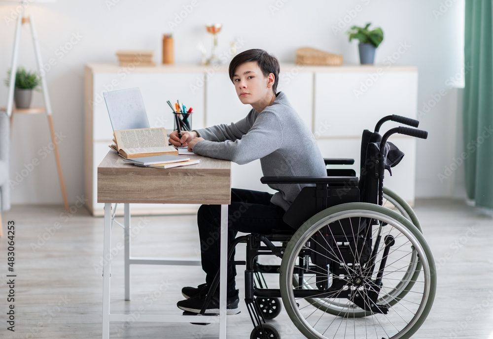 Disabled teenager in wheelchair learning online with books and laptop computer at home Disabled teenager in wheelchair learning online with books and laptop computer at home