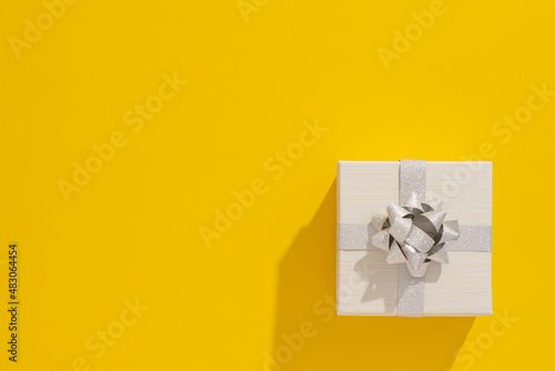 
One grey gift box with silver ribbon and bow on yellow table background. Minimal festive gift background. Top view. Flat lay.