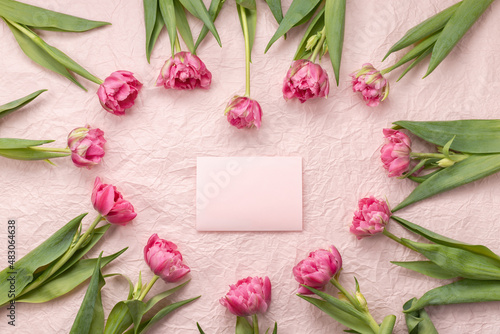 Fototapeta Naklejka Na Ścianę i Meble -  Frame of tulips laid out in the shape of a heart on a pale pink background and an empty postcard with a place for the text of congratulations on Valentine's Day, mother's day or birthday.
