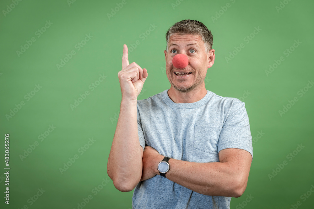 man with red clown nose and grey shirt in front of green background man with red clown nose and grey shirt in front of green background