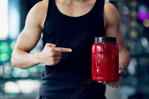 Bodybuilding Supplements. Muscular Man Pointing At Red Container With Whey Proteing Powder photo