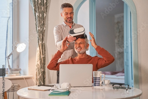 Adult son and his senior father with VR goggles at home