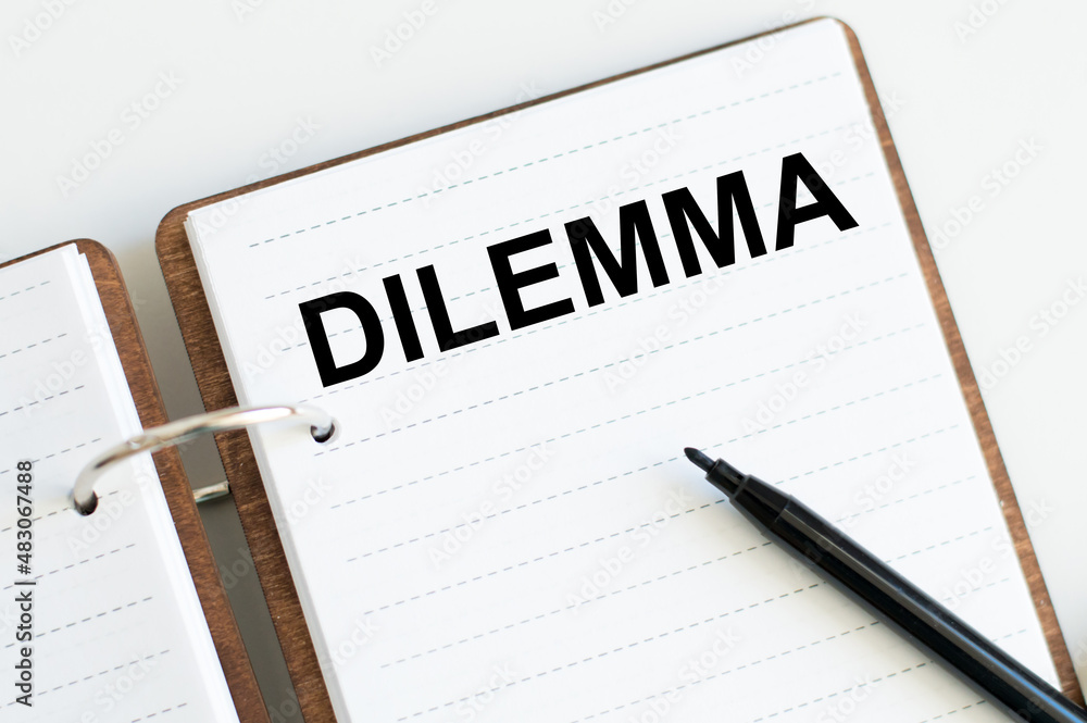 text DILEMMA on an open notepad on a table next to a black marker, a business concept text DILEMMA on an open notepad on a table next to a black marker, a business concept