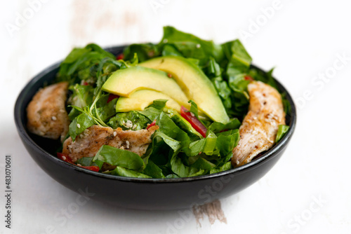 Healthy  vegetable buddha bowl salad with fried chicken and avocado, peppers and leaf lettuce on a white plate.