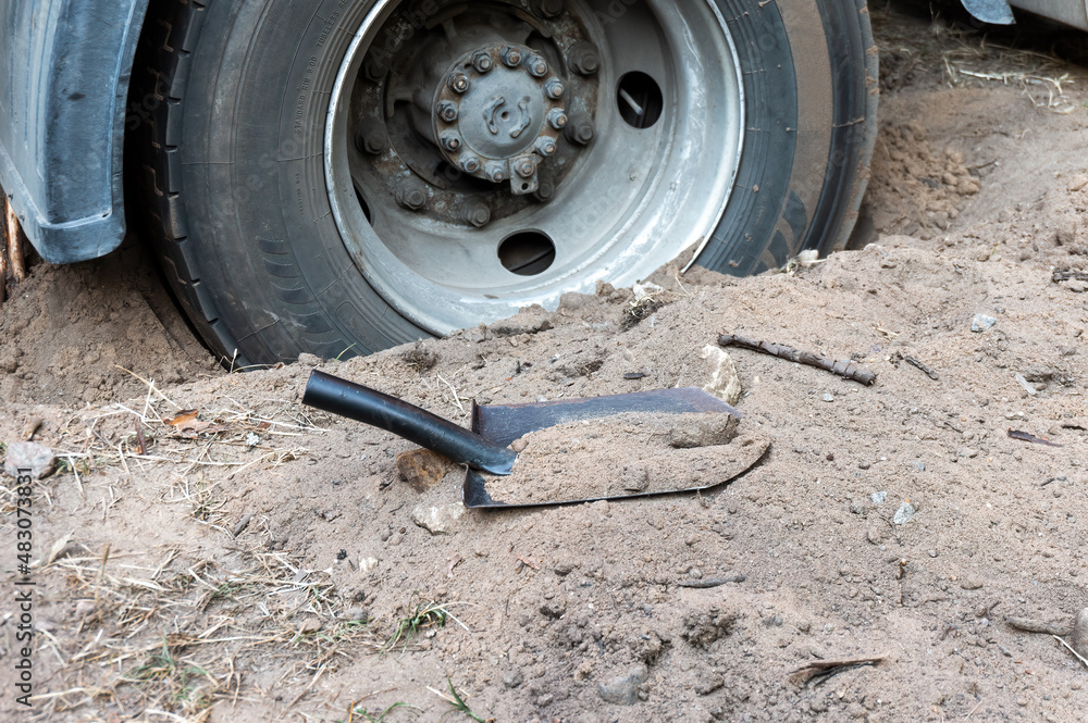 Truck wheel is stuck in the sand. Shovel nearby. Truck wheel is stuck in the sand. Shovel nearby.