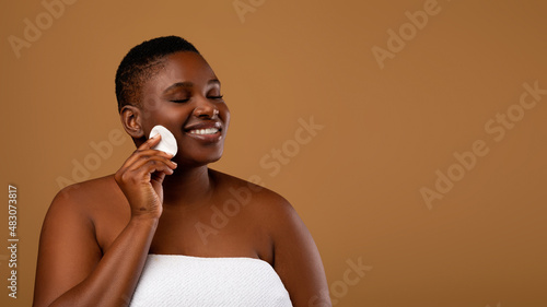 Portrait of curvy black woman cleaning skin by cotton pad photo