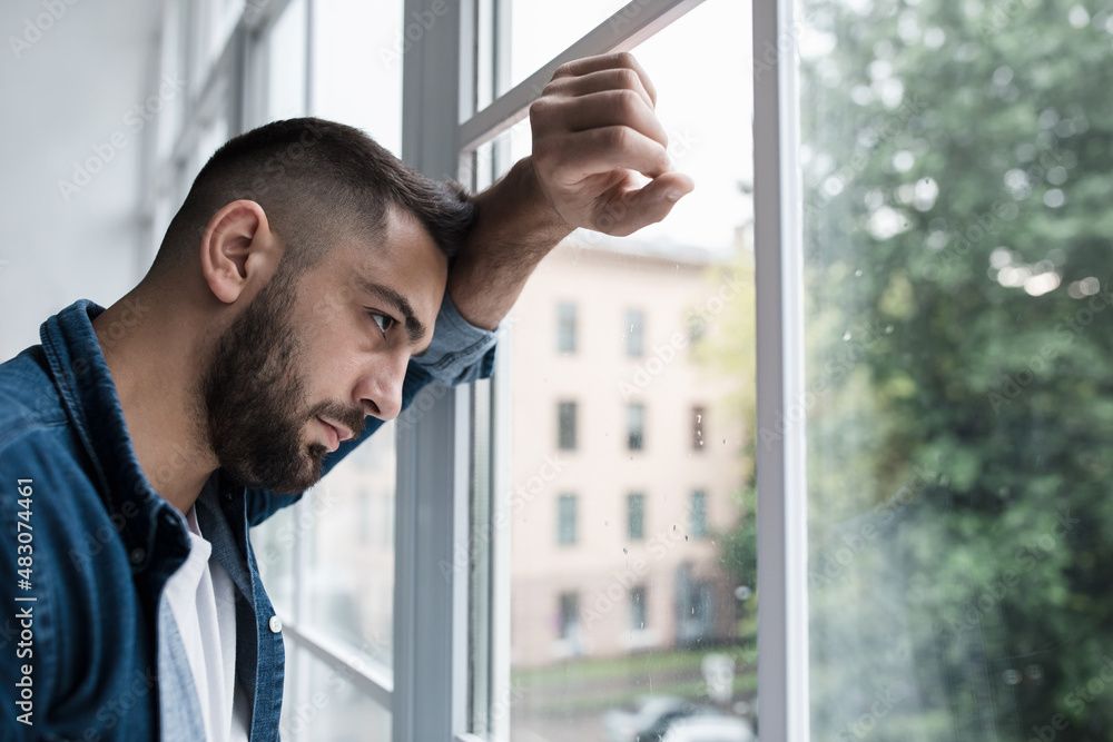 Sad unhappy young handsome man with hand on glass in kitchen interior Sad unhappy young handsome man with hand on glass in kitchen interior