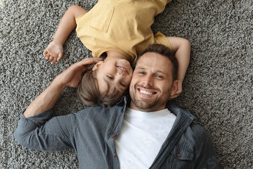 Happy dad and son. Top view of young positive father and his little son smiling at camera, lying on carpet floor