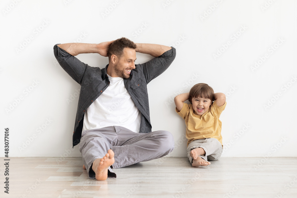 Relax time. Happy little boy sitting with daddy and laughing to camera, leaning wall with hands behind head Relax time. Happy little boy sitting with daddy and laughing to camera, leaning wall with hands behind head