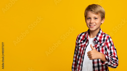 Cheerful confident european teen boy showing thumb up looking at camera, on yellow background