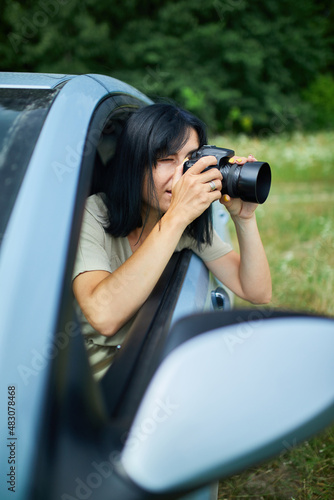 Woman photographer sitting in the car and photographing a flower field landscape © bondarillia
