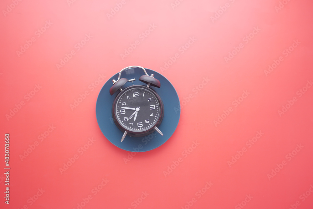 Alarm clock on plate on red background top down 